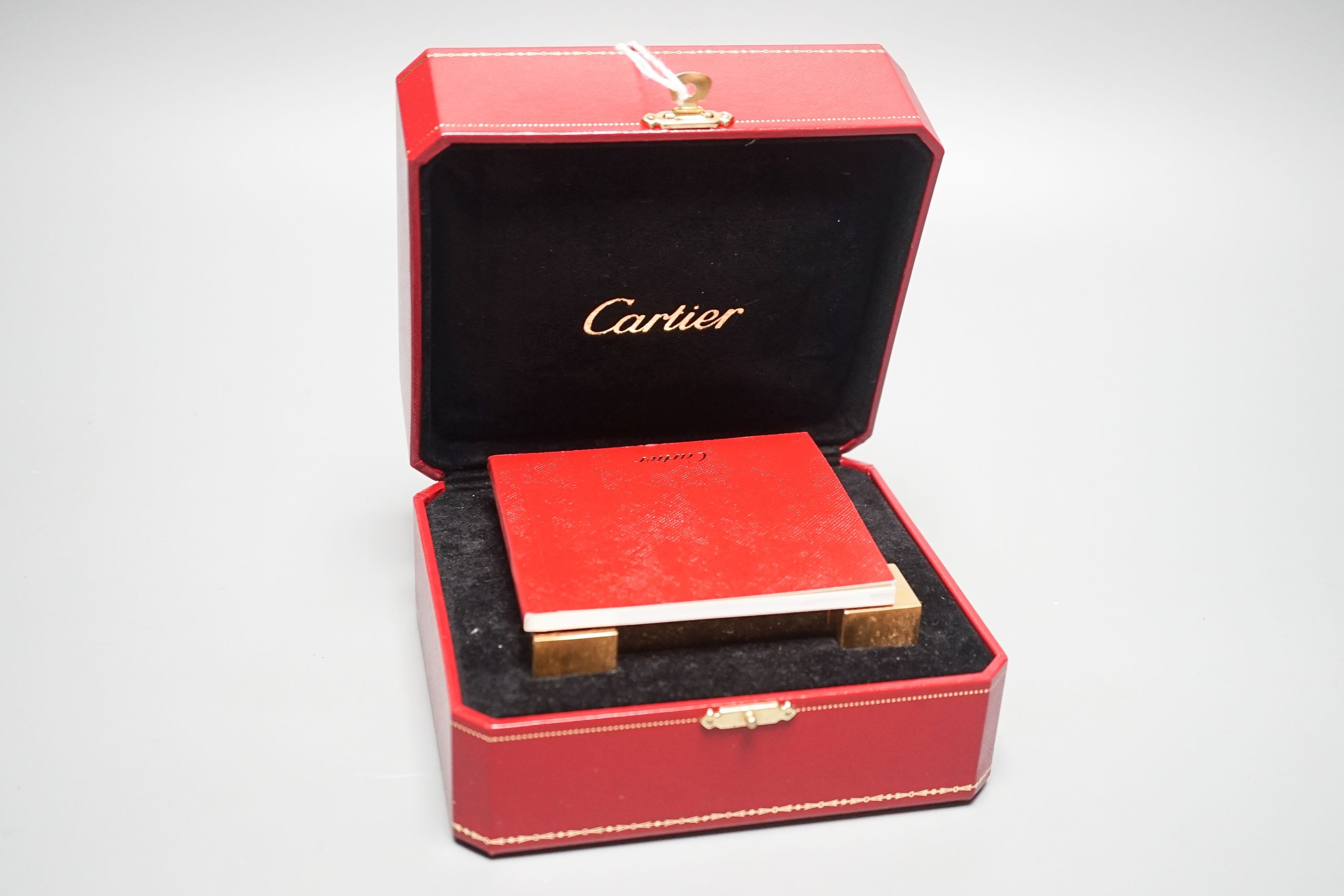 A cased Cartier gilt metal travelling clock, 10.5 cm wide, with certificate booklet